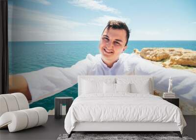 Handsome young man taking a selfie from camera on vacation on ocean and cliff background Wall mural